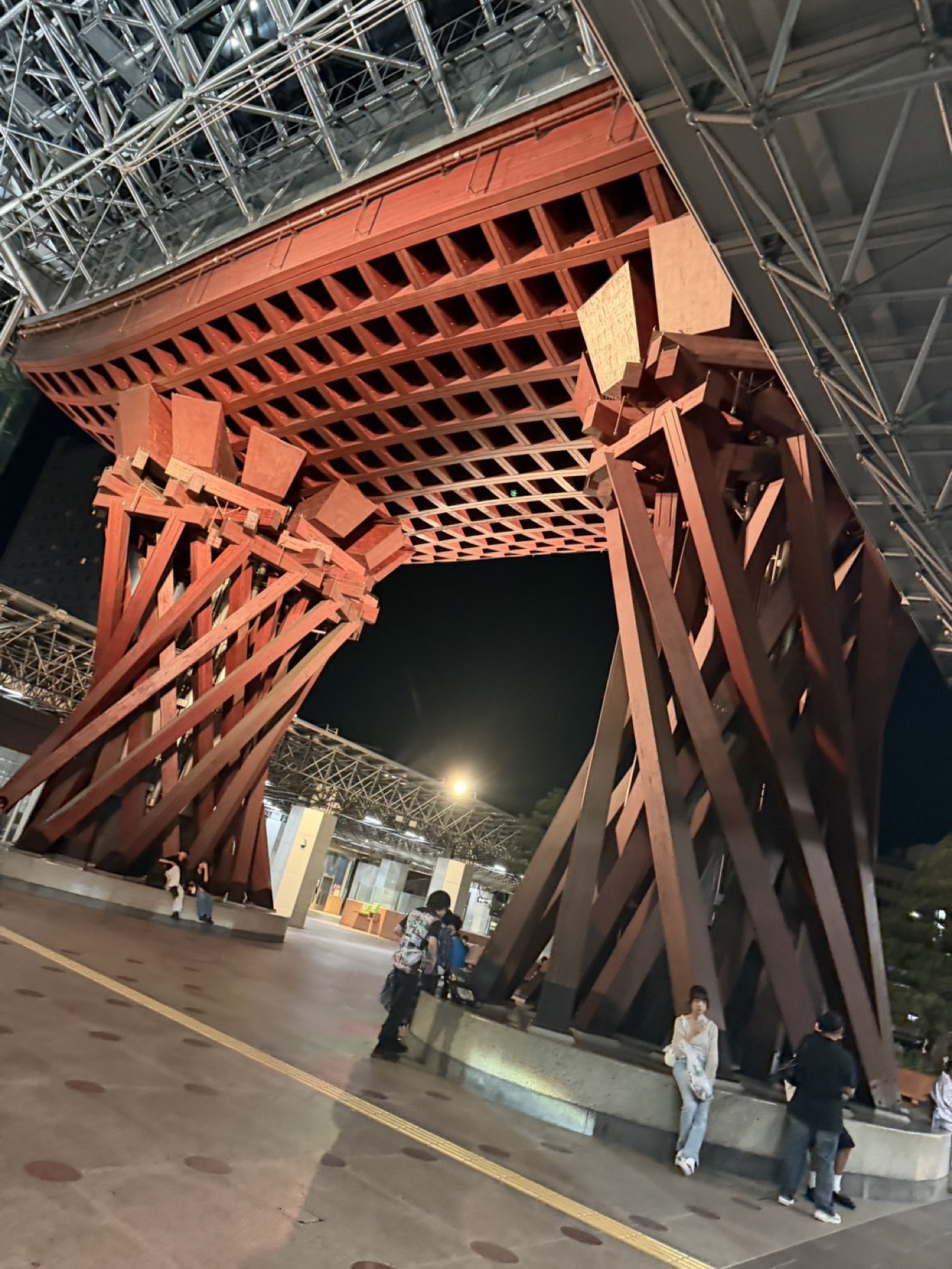 夜の金沢駅・鼓門を見上げたところ。柱のそばで人が待っている
